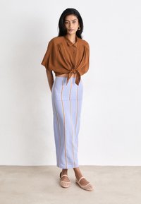 Brown short-sleeve button-up shirt tied at the waist, paired with a light blue knee-length skirt featuring vertical stripes and soft pink flats.