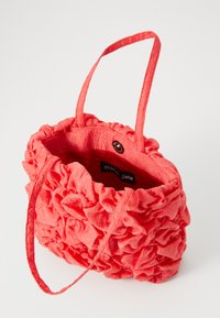 Borsa a mano in tessuto corallo con ruffles testurizzati, due manici sottili e chiusura con bottone. L'interno è foderato con l'etichetta del marchio.