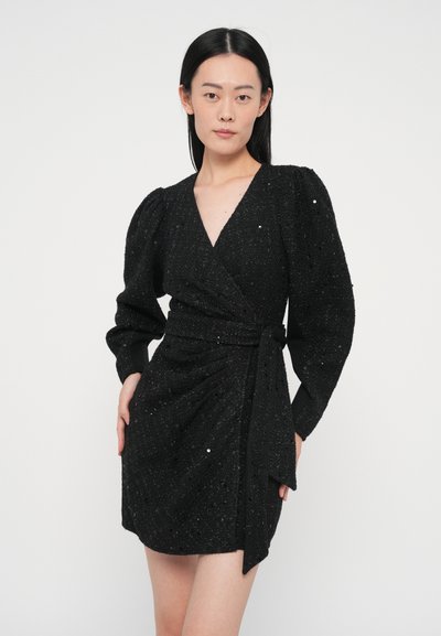 Melnas apvijas kleita ar gariem pūkainiem piedurknēm, teksturētu audumu un izrotāta ar spīdumiem. Raksturīga jostas sasiešanas detaļa un īsāks garums.