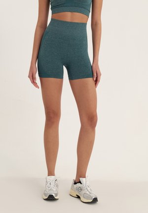 Teal actieve shorts met een hoge taille, gemaakt van textielstof, gecombineerd met witte en zilveren sportschoenen. Korte lengte en aansluitend ontwerp.
