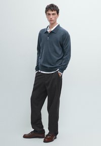 Námořnický pulover s límcem, nošený přes bílou košili; spárován s volnými černými kalhotami a hnědými šněrovacími botami.