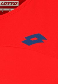Top deportivo rojo sin mangas con una textura suave, que presenta un logo azul de Lotto en el escote, ofreciendo un diseño elegante y moderno.