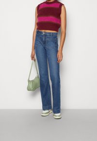 Haut en tricot sans manches bordeaux avec des rayures roses et vertes, associé à un jean taille haute bleu, un sac à main vert et des baskets avec des accents verts.