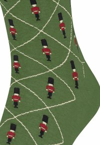 Zielone skarpetki z powtarzającymi się ilustracjami żołnierzy-zabawek w czerwonych mundurach, czarnych kapeluszach i białych akcentach, tworzącymi zabawny wzór.