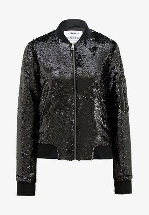 Black bomber jacket covered in sequins, featuring a zip front, ribbed cuffs, and a collar. Detailed with a zippered pocket on the sleeve.