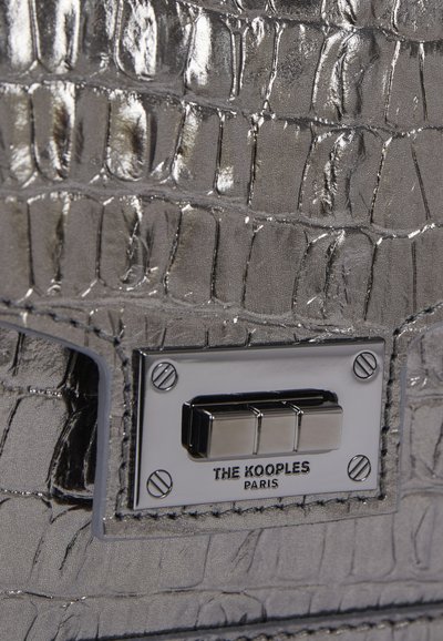 Silberne Tasche mit Krokodilleder-Textur, ausgestattet mit einem Metallverschluss und einem Logo-Schild. Die glatte Oberfläche und die detaillierte Naht verleihen dem Design zusätzlichen Charme.