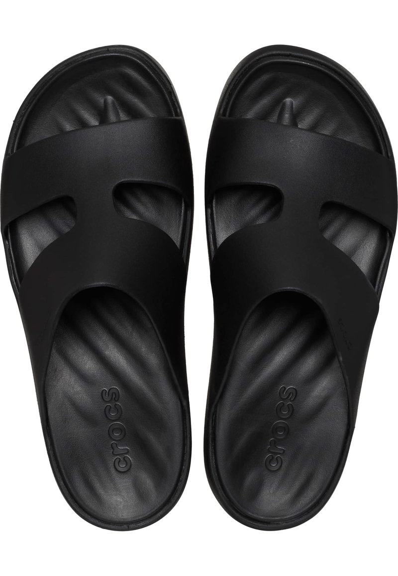Des sandales noires à enfiler avec deux larges sangles, fabriquées en matériau texturé, dotées d'un matelas de pied ergonomique et de la mention "crocs" embossée à l'intérieur.