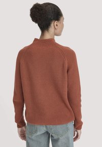 Rustfarbenes Sweatshirt mit gerippter Textur und hohem Kragen. Verfügt über lange Ärmel und einen lockeren Schnitt, kombiniert mit hellblauen Jeans.