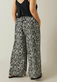 Zwart-wit gestreepte breed-pant met een elastische tailleband. De stof heeft ingewikkelde bloempatronen. Zakjes zijn zichtbaar.