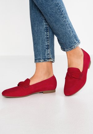 Mocassins en daim rouge avec un détail noué, semelle plate et texture lisse, associés à des jeans bleus retroussés.