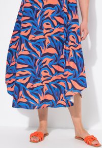 Vestido maxi con estampado de motivos de hojas en rosa, azul y marino; tejido suave; dobladillo asimétrico. Combinado con sandalias de tiras naranjas.