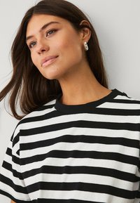 T-shirt à rayures noires et blanches avec des manches courtes, un col rond et une coupe décontractée. Texture lisse et sans motifs ni accents visibles.