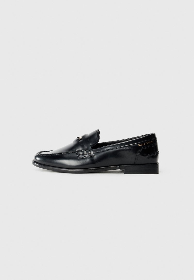 Mocassin homme en cuir noir avec talon bas et détails de couture, présenté de côté sur un fond gris clair uni.