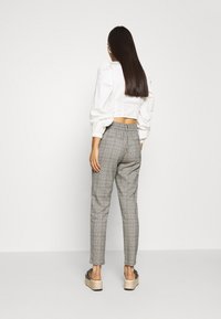 Witte cropped blouse met pofmouwen, gecombineerd met grijze geruite broek. De broek heeft een elastische tailleband en een taps toelopende pasvorm. Sleehak sandalen.