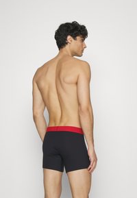 Svarta boxershorts med röd midja, som har en tight passform och en mjuk textur. Vy från baksidan som framhäver designen och midjan.