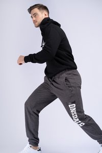 Sudadera con capucha negra y pantalones de chándal grises con logo. Los pantalones de chándal tienen bolsillos laterales y un ajuste relajado, combinados con zapatillas deportivas blancas.
