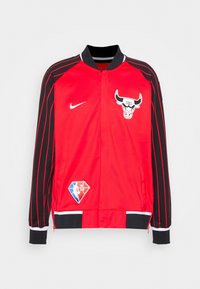 Red Nike jacket with black sleeves, features a Chicago Bulls logo, side pockets, and striped accents. Ribbed cuffs and collar detail included.