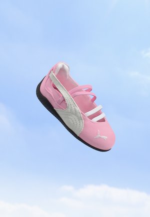 Baskets pour enfants rose et blanc avec une semelle noire flottant devant un ciel bleu avec de légers nuages.