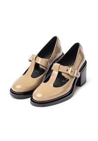 Chaussures en cuir verni beige avec une bride en T, détail boucle et un talon noir épais. Présente une ouverture à l'avant et un design découpé.