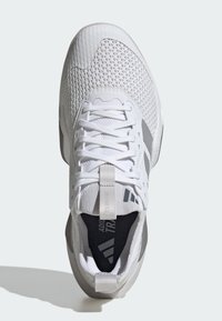 Hvid sportssko med meshniveau, flade snørebånd og tekstureret tåafsnit. Grå accenter på siden og en trækflig på hælen.