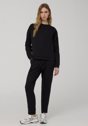 Felpa nera con maniche lunghe, vestibilità morbida e scollatura rotonda, abbinata a pantaloni tapered coordinati e scarpe sportive argentate.
