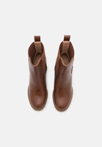 Brązowe skórzane botki za kostkę o gładkiej fakturze, z elastycznymi panelami bocznymi i pętelkami do łatwego zakładania. Podeszwa ma lekko wygięty przód.