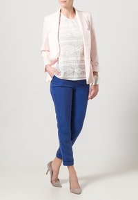 Světle růžový blazer, bílý vyšívaný top a modré zúžené kalhoty. Šedé vysoké podpatky. Hladké textury, strukturovaný design a kontrastní barvy.