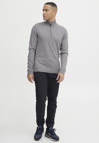 Grauer Zip-Kragen-Pullover, mit gerippten Bündchen und Saum, getragen mit dunklen Hosen und marineblauen Sneakers. Glatte Textur, schlanker Schnitt und lässiger Stil.
