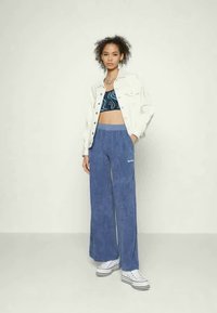 Calças largas azul claro feitas de um tecido texturizado, combinadas com um top crop padrão preto e azul e uma jaqueta de ganga branca.