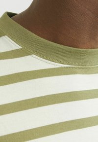 Camiseta de rayas verde oliva y crema; tejido suave de punto; cuello acanalado; primer plano del escote y área del hombro.