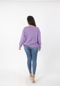 Paarse gebreide trui met een losse pasvorm, verlaagde schouders en geribbelde manchetten, gecombineerd met blauwe skinny jeans en doorzichtige hakken.