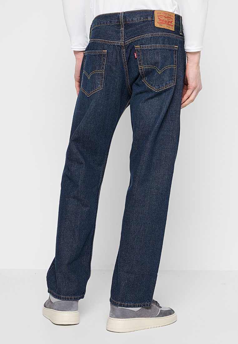 Jean en denim bleu foncé à coupe droite, avec un patch en cuir à la taille et des poches arrière avec des accents de couture.