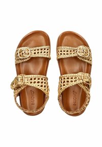 Zlaté tkané sandály s dvěma nastavitelými pásky, hladkým hnědým stélkou a mírným podpatkem. Obsahují dekorativní spony a chunky, texturovaný design.