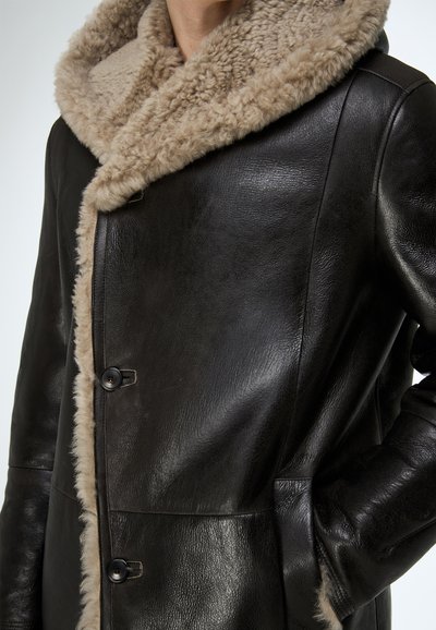 Schwarzer Ledermantel mit einem weichen beigen Lammfellkragen, ausgestattet mit Knopfverschluss und Seitentaschen, glatter Textur und klaren Linien.