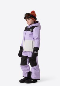 Lilla og svart isolert skijakke med matchende bukser. Har en hvit panel, tykke hansker og en rød strikkelue med dusk.