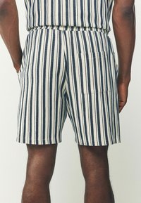 Shorts rayés présentant un motif marine et ivoire, fabriqués à partir d'un tissu texturé, avec une taille élastique et des poches latérales.