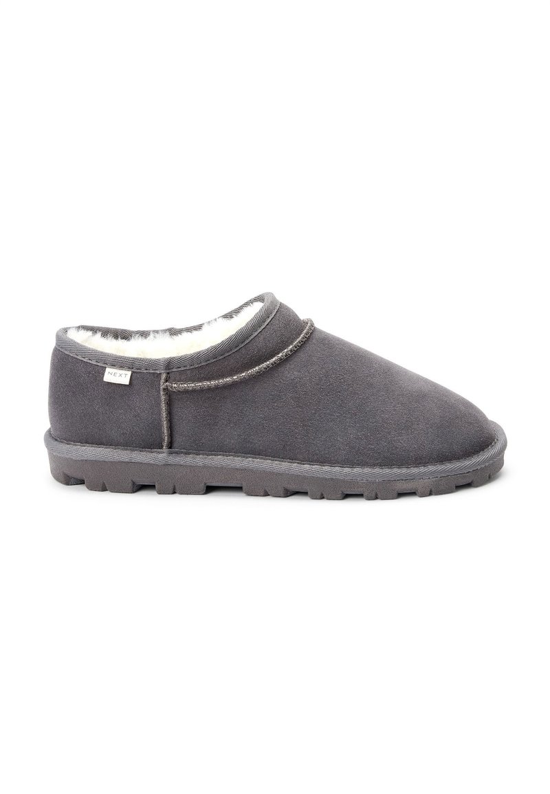 Grå ruskindsmooth slippers med blødt, hvidt fleecefor, rund tå og en tekstureret gummisål. Fremhævet syningdetalje langs overdelen.