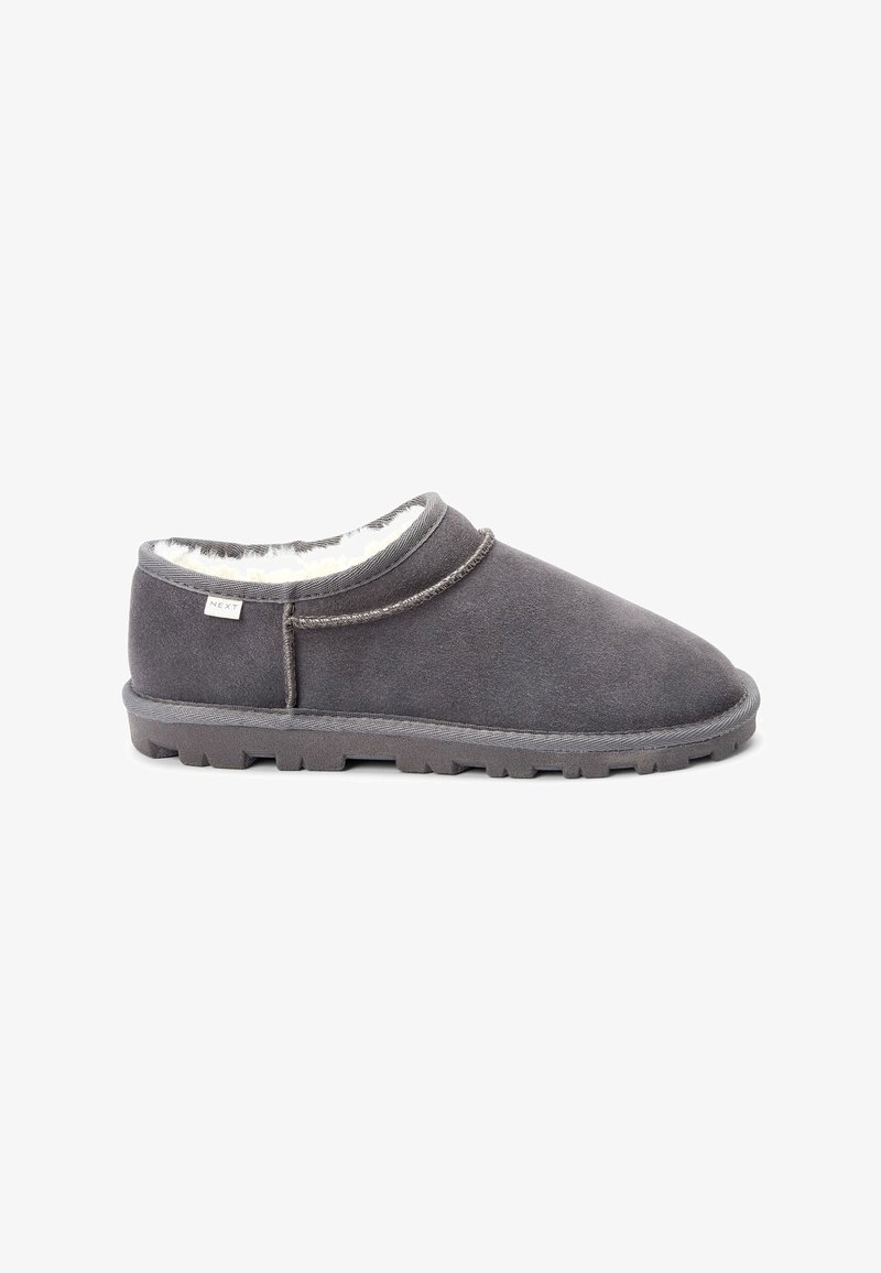 Pantofole grigie in suede con morbida fodera in pile bianco, punta arrotondata e suola in gomma texturizzata. Dettaglio di cucitura evidenziato lungo la parte superiore.