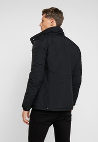 Black puffer jacket with a high collar, featuring quilted texture and snap button accents. Simple, streamlined design. Machine washable.