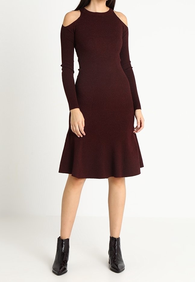 Robe bordeaux à côtes avec découpes aux épaules dénudées, manches longues, corsage ajusté et jupe évasée, associée à des bottines noires à la cheville.