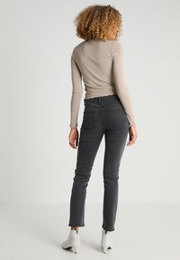 Jeans negros ajustados de mezclilla, con cintura alta, bolsillos traseros y una blusa de manga larga texturizada y acanalada en color beige.