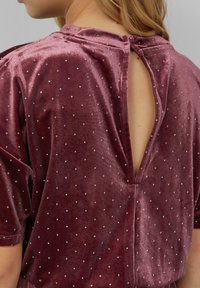 Burgundské sametové tričko s krátkymi rukávmi, so strihom na chrbte v tvare kľúčovej dierky a striebornými bodkovými ozdobami po celej látke.