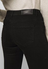 Jeans de mezclilla negros elásticos con cintura de altura media, que cuentan con dos bolsillos traseros y un parche de cuero liso de la marca en la cintura.