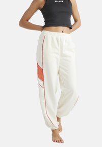 Vita sweatpants med en orange accent och röda detaljer. Har en elastisk midja och avsmalnande ärmslut. Bärs med en svart croppad topp.