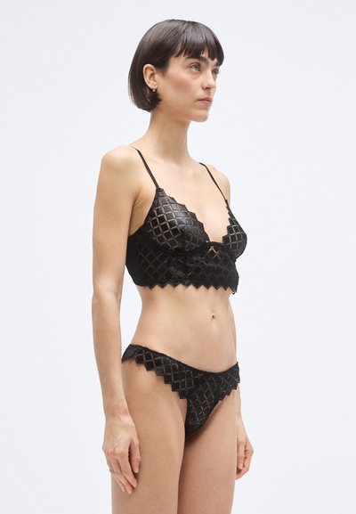 Čierna sada spodnej bielizne obsahujúca textúrovaný bralet s diamantovým vzorom, nastaviteľnými ramienkami a zodpovedajúce bikiny so zubatými okrajmi.
