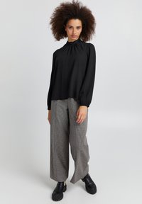 Blusa nera a maniche lunghe con colletto alto, abbinata a pantaloni a gamba larga a scacchi e stivaletti neri robusti. Tessuto morbido, vestibilità casual.