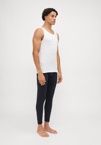 Weißes ärmelloses Tanktop und schwarze eng anliegende Jogginghosen aus weichem Stoff, präsentiert an einer stehenden Figur mit lockigem Haar.