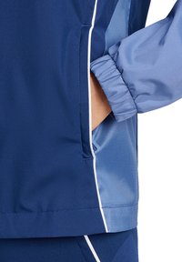 Marineblaues Jacket aus strukturiertem Material mit hellblauen Akzenten, elastischen Bündchen und einer Seitentasche mit glatter Oberfläche.