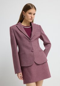 Vævet houndstooth-mønster blazer i burgunder med matchende nederdel. Har klippede revers, to knapper og forlommer. Glat tekstur.