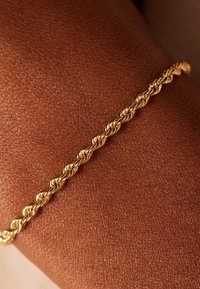 Gold twisted chain bracelet resting on textured brown skin, showcasing a braided design and shiny finish with visible links.